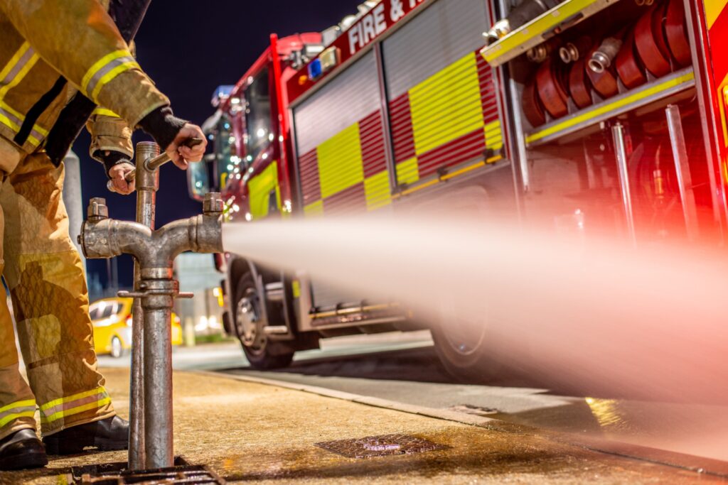 Firefighter operating a hydrant standpipe beside a fire engine at night